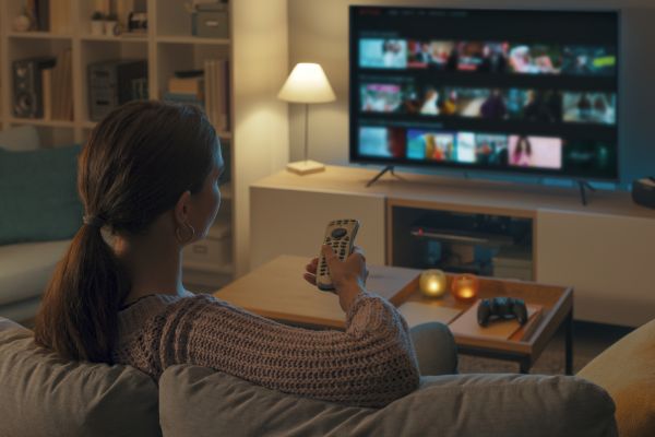 Photo of a woman using a remote to select content to watch on a TV