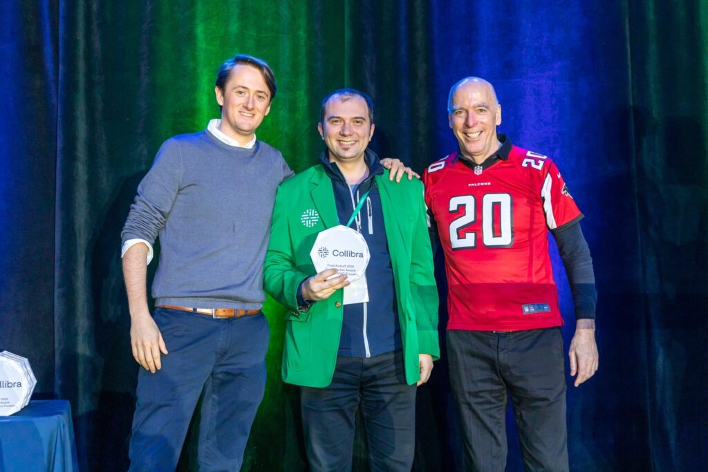 Sales engineer Tudor Borlea holds an award and wears an iconic green Collibra jacket while standing beside Felix Van de Maele and another person