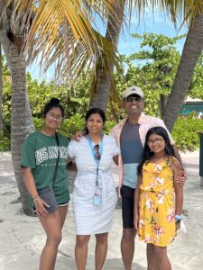 Collibra Senior Software Engineer Vidhya Sitaraman smiles with her husband and two daughters in a tropical location