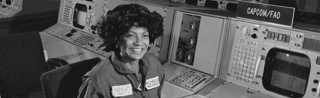 Nichelle Nichols smiles as she sits behind a NASA computer board